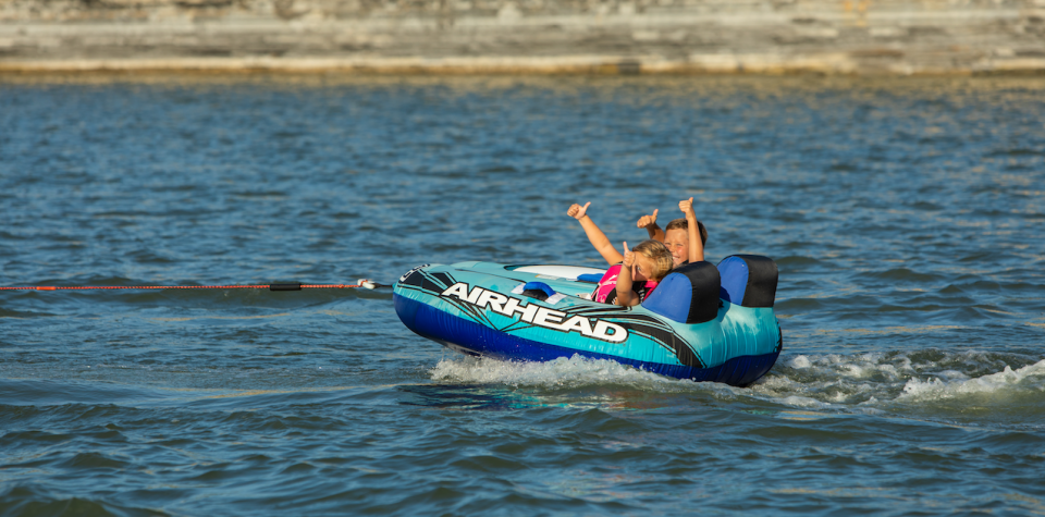 Kids being pulled by a boat while sitting in a tube giving thumbs up